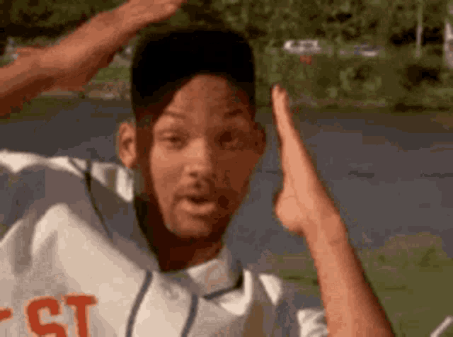 a man in a baseball uniform is standing in front of a lake with his hands in the air .