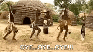 a group of native americans are dancing in front of a thatched hut .