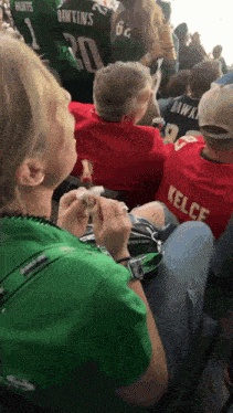a woman in a green shirt is sitting next to a man in a red shirt with the name kelce on it