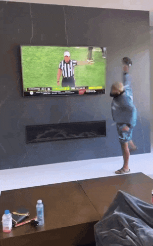 a man is standing in front of a television watching a football game