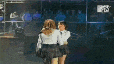 two girls in school uniforms are hugging each other on a stage with a mtv logo in the background