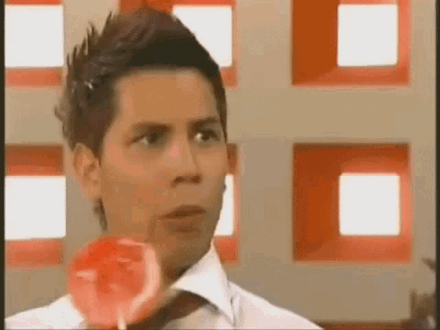 a young man in a white shirt and tie is holding a red lollipop .