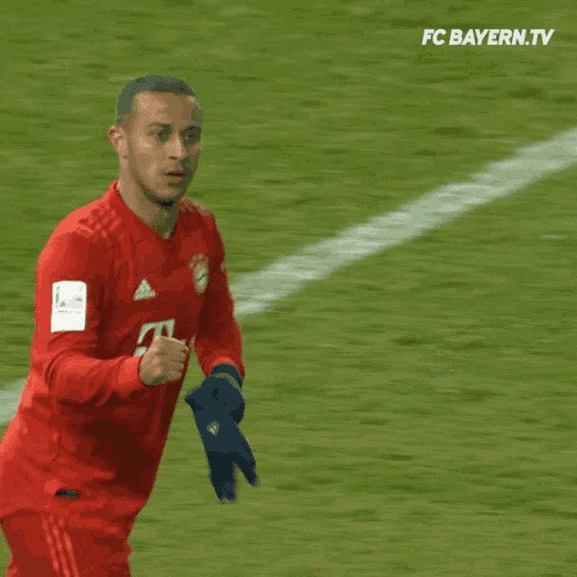 a man in a red t-mobile jersey stands on a soccer field sponsored by fc bayern.tv