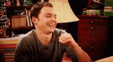 a man is laughing while sitting at a table in a room .