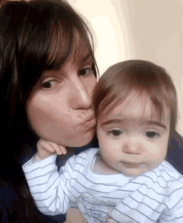 a woman is kissing a baby on the cheek and the baby is wearing a striped shirt