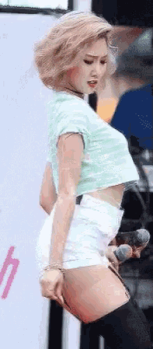 a woman in a crop top and white shorts is holding a microphone and dancing on a stage .