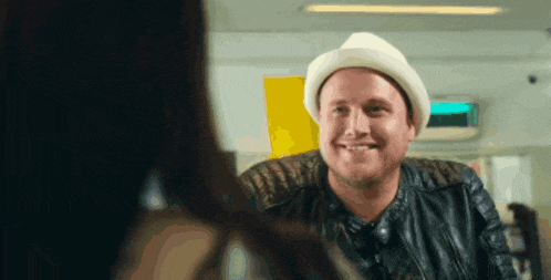 a man wearing a hat and a leather jacket is smiling while looking at a woman .