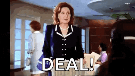 a woman in a suit and pearl necklace is standing in front of a sign that says deal !