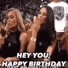 two women are sitting in the stands at a basketball game and one is blowing a kiss .
