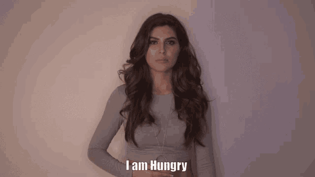 a woman says i am hungry in front of a white wall