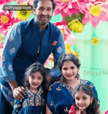 a family posing for a picture in front of a wall of pink flowers .