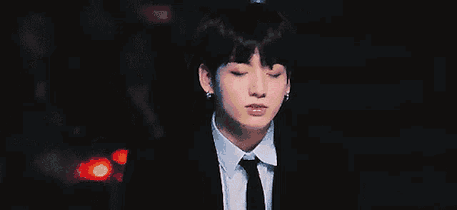 a man in a suit and tie is standing in the dark with his eyes closed .