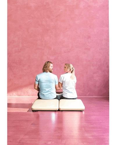 a man and a woman sit on a pink floor