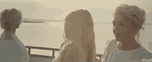 three women are standing next to each other on a boat looking at the water .