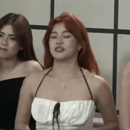 a woman with red hair is wearing a white halter top and a necklace .