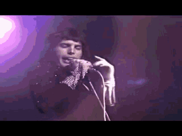 a man is singing into a microphone on a stage while wearing gloves .