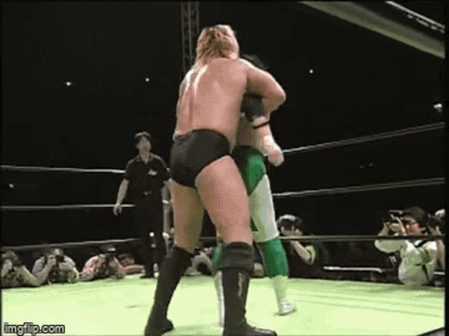 two wrestlers are fighting in a wrestling ring with a referee watching .