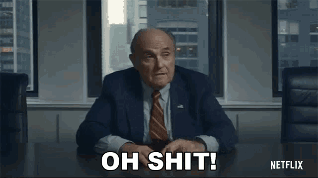 a man in a suit and tie is sitting at a table and saying `` oh shit ! ''