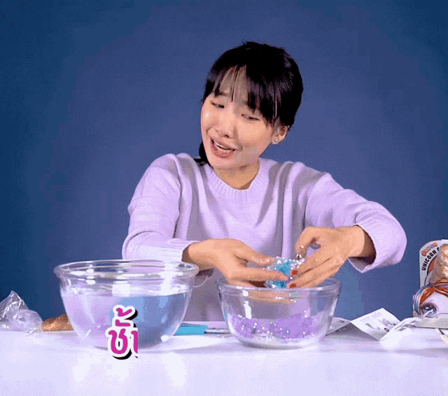 a woman in a purple sweater sits at a table with bowls of water and a sticker that says ok