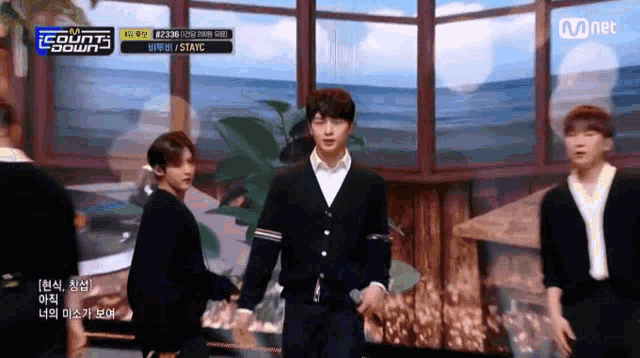 a group of young men are standing on a stage in front of a window with a mnet logo above them .