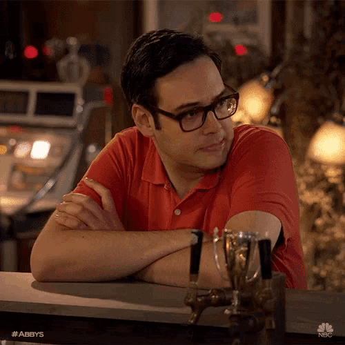 a man wearing glasses and a red shirt is leaning on a counter with a trophy on it