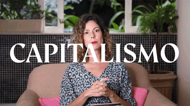 a woman sits on a couch in front of a sign that reads capitalismo
