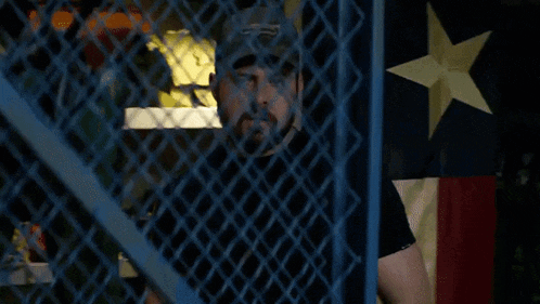 a man wearing a hat and a watch is standing behind a chain link fence .
