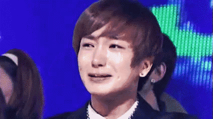a young man is crying on a stage while wearing a suit and tie .