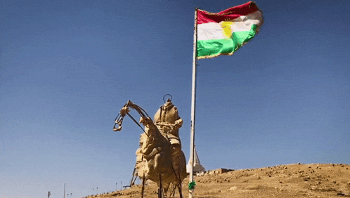 a statue of a man riding a horse in front of a flag that says kurdistan