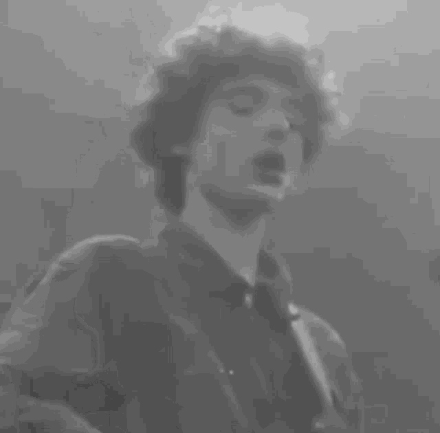 a black and white photo of a man with curly hair in a dark room .