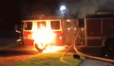 a fire truck is on fire at night with flames coming out of the front of it .