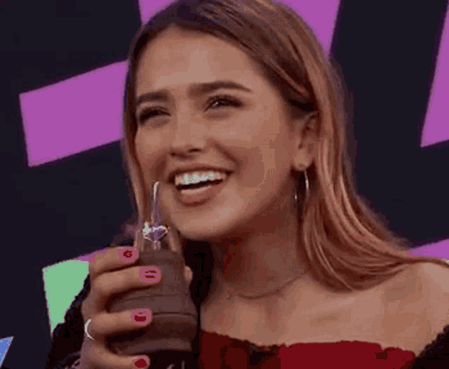 a woman with red nails is smiling while holding a glass of water .
