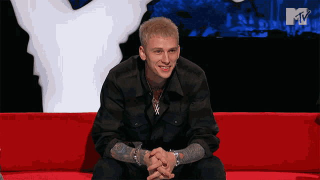 a man is sitting on a red couch in front of a tv screen that says mtv