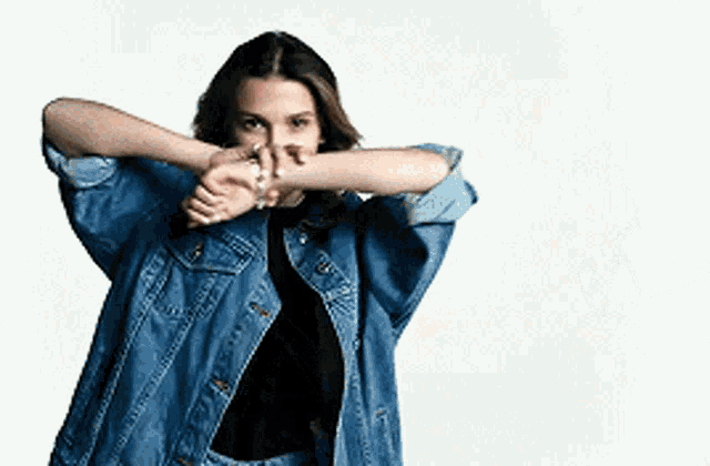 a woman wearing a denim jacket and a black shirt is stretching her arms .
