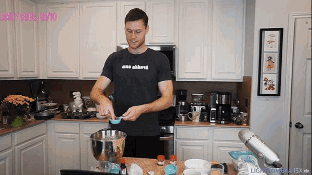 a man wearing a black shirt that says daily subs 13/13 is preparing food in a kitchen