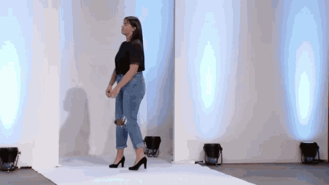 a woman is walking down a runway wearing jeans and high heels