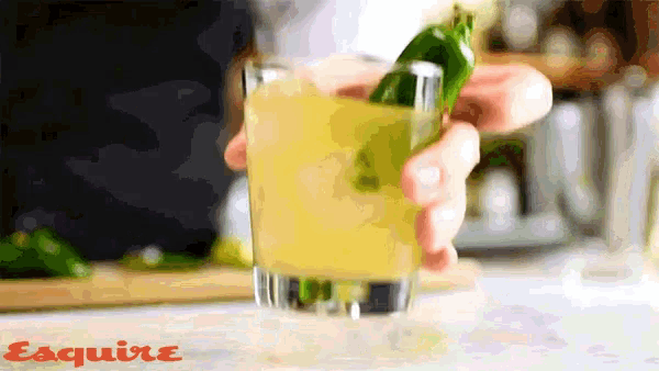 a person is holding a green pepper in a glass with esquire written on the bottom of the image