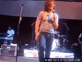 a man singing into a microphone on a stage with a make gifs at gifsoup.com watermark