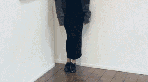 a woman wearing a black skirt and black shoes is standing in a corner .