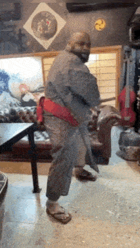 a bald man in a kimono is standing in a living room .