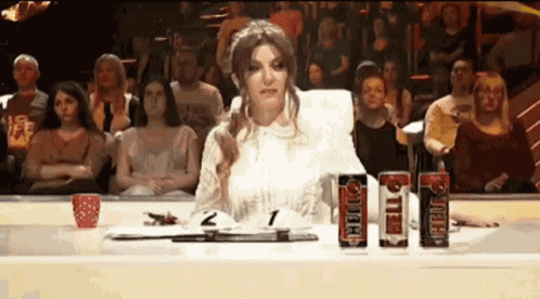 a woman is sitting at a table in front of a crowd with two cans of tiger sitting on it .