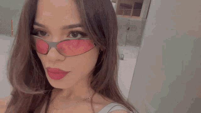 a woman wearing a pair of pink sunglasses looks at the camera