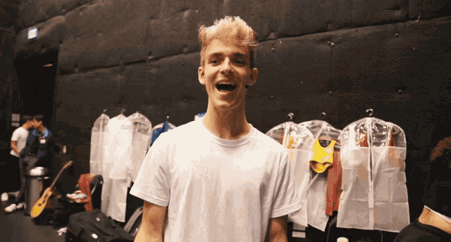 a young man in a white shirt is standing in front of clothes hanging on a rack and smiling