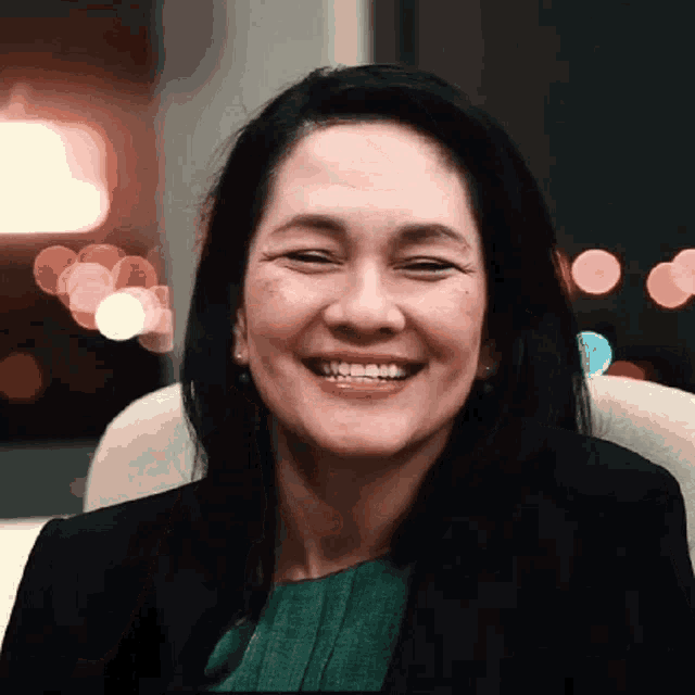 a woman in a green shirt and black jacket is smiling for the camera .