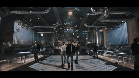 a group of people are dancing in a large room with a lot of pipes hanging from the ceiling .