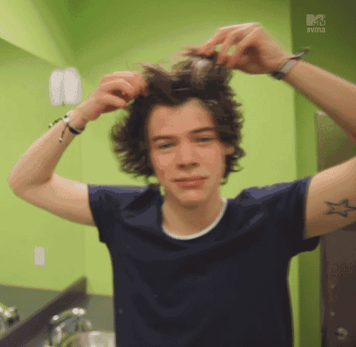 a young man combs his hair in front of a green wall that says mtv evm3