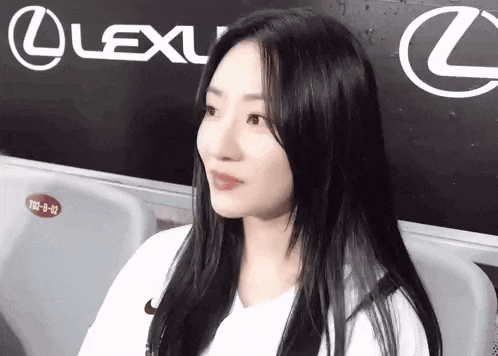 a woman with long black hair is sitting in front of a lexus advertisement .