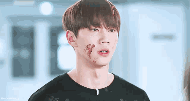 a young man with blood on his face is wearing a black t-shirt with the letters t on it