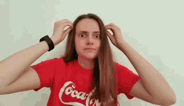 a woman is wearing a red coca cola shirt and holding her hair .