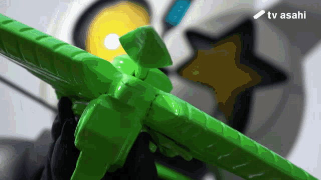a person is holding a green toy with a tv asahi logo in the corner